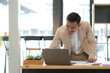 © wichayada - Young Asian businessman in suit working with laptop computer in office. Man in suit using laptop in well-lit workplace.