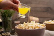 Melted butter being poured on popcorn in clay bowl on kitchen table