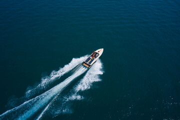 Wall Mural - Luxurious boat fast movement on dark water. Luxurious  motor boat rushes through the waves of the blue Sea. Boat fast moving aerial view.