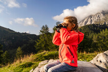 Girl Looking Through Binoculars Sitting On Rock