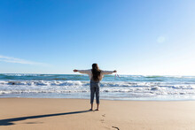 Girl With Arms Outstretched Looking At Horizon Over Sea