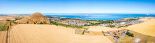 UK, Scotland, North Berwick, Aerial Panorama Of Vast Wheat Field In Front Of Coastal Town In Summer