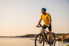 Mature Man Riding Bicycle On Shore At Sunset