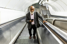 Bald Senior Commuter With Mobile Phone Moving Up On Escalator