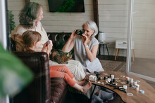 Woman Taking Photo Of Senior Man And Granddaughter On Vintage Film Camera At Home