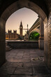 Big Ben and the Houses of Parliament, framed by an ancient, stone archway, across the river Thames