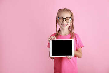 smiling funny child girl with tablet in hands on pink background. Caucasian school kid in glasses showing empty screen and looking in camera. Advertisement blank. Pupil promote product.