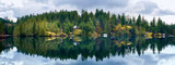 Fototapeta Góry - Houses on the rocks among the coniferous forest are reflected in the crystalline water of the wild Ruby Lake in calm weather. Forest landscape at Dan Bosch Park, Sunshine Coast Hwy, BC, Canada
