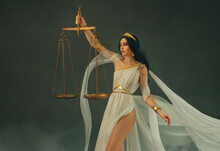 Portrait Fantasy Woman Greek Goddess Of Justice Themis, Holding Golden Scales In Hands. White Silk Vintage Dress Old Antique Style Flies Waving In Wind. Girl Sexy Virgo Astrology Zodiac Sign Art Photo