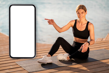 Middle Aged Sporty Woman Pointing At Big Blank Smartphone While Training Outdoors