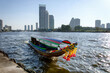 Traditional colorful long-tail boat sailing on the Chao Phraya river surrounded by modern skyscrapers in the background.