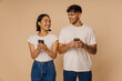 Young multiracial couple smiling and using mobile phones