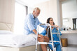 © chokniti - Portrait of Asian young nurse helping old elderly disable man grandfather to walk by using walker equipment in the bedroom. Senior patient of nursing home moving with walking frame and nurse support