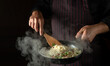 The cook prepares delicious spaghetti with spices and seasonings in a steamed hot frying pan. Space for advertising on a dark background. Menu for a restaurant or hotel.