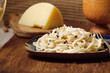 Cacio e Pepe - Italian pasta with grated Pecorino Romano cheese and black pepper, together with spaghetti in a black plate on wooden background. Close up,  flat lay, copy space.