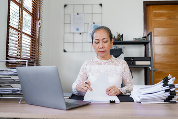 Attractive mature asian business woman working on laptop at her workstation.