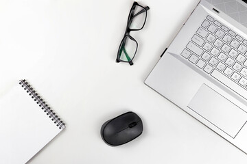 Poster - A blank notebook with glasses a computer mouse and a laptop are on a white table. Top view with copy space