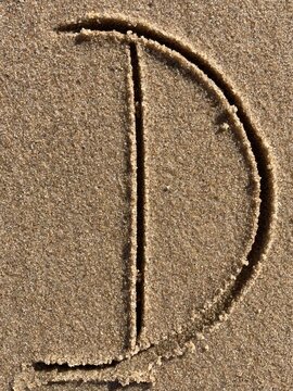 On the beach in the sand is carved the letter D