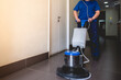 Young latino janitorial worker lady in blue uniform cleaning in building with industrial vacuum cleaner