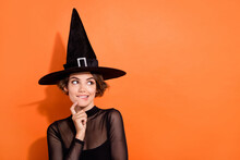 Photo Portrait Of Pretty Young Lady Bite Lip Look Empty Space Wear Stylish Black Halloween Witch Garment Isolated On Orange Background