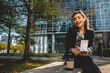 © Samuel Ponce - Young, successful and happy latina businesswoman with sunglasses and a cup of coffee taking notes of their ideas in a notebook in a park between skyscrapers