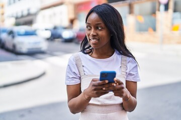 Wall Mural - Young african american woman smiling confident using smartphone at street