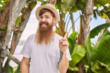 Canvas Print - Caucasian man with long beard outdoors on a sunny day wearing summer hat smiling happy pointing with hand and finger to the side