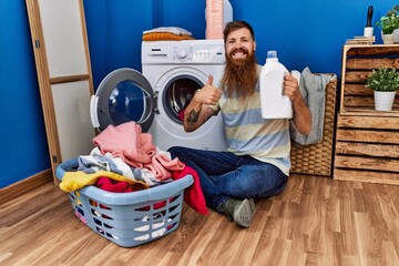 Sticker - Redhead man with long beard doing laundry holding detergent bottle smiling happy and positive, thumb up doing excellent and approval sign