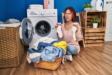 Poster - Young caucasian woman doing laundry holding socks angry and mad screaming frustrated and furious, shouting with anger. rage and aggressive concept.