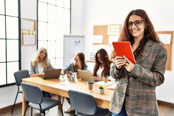 Wall Mural - Young businesswoman smiling happy using touchpad while partners work at the office.