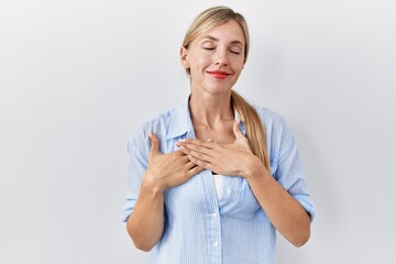 Sticker - Beautiful blonde woman standing over white background smiling with hands on chest with closed eyes and grateful gesture on face. health concept.