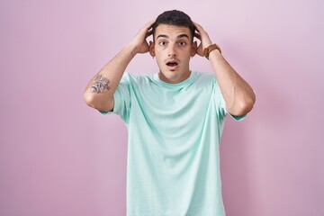 Wall Mural - Handsome hispanic man standing over pink background crazy and scared with hands on head, afraid and surprised of shock with open mouth