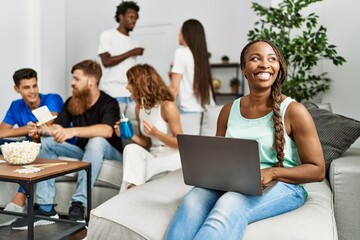 Wall Mural - Group of young friends smiling happy sitting on the sofa. Woman using laptop at home.