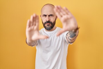 Sticker - Young hispanic man with tattoos standing over yellow background doing frame using hands palms and fingers, camera perspective