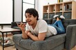 © Krakenimages.com - Young hispanic man talking on the smartphone lying on the sofa at home.