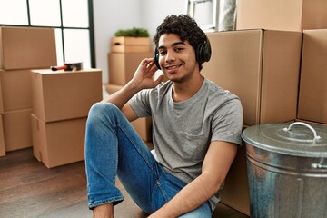Canvas Print - Young hispanic man listening to music sitting on the floor at new home.