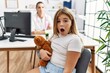 Blonde little girl at pediatrician clinic with female doctor scared and amazed with open mouth for surprise, disbelief face