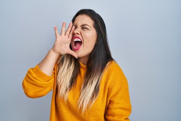 Wall Mural - Young hispanic woman standing over isolated background shouting and screaming loud to side with hand on mouth. communication concept.