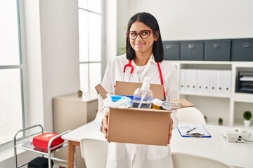 Canvas Print - Young hispanic doctor woman holding box with medical items smiling looking to the side and staring away thinking.