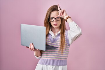 Sticker - Young caucasian woman working using computer laptop making fun of people with fingers on forehead doing loser gesture mocking and insulting.