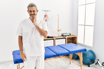 Poster - Middle age hispanic therapist man working at pain recovery clinic touching mouth with hand with painful expression because of toothache or dental illness on teeth. dentist