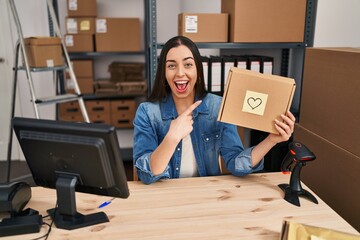 Canvas Print - Hispanic woman working at small business ecommerce holding box smiling happy pointing with hand and finger