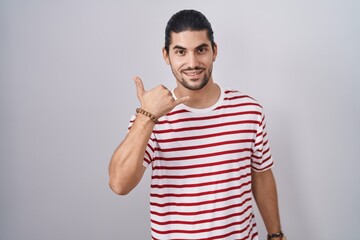 Wall Mural - Hispanic man with long hair standing over isolated background smiling doing phone gesture with hand and fingers like talking on the telephone. communicating concepts.