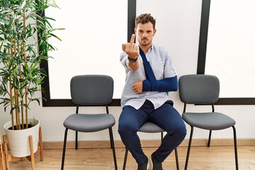 Sticker - Handsome young man sitting at doctor waiting room with arm injury showing middle finger, impolite and rude fuck off expression