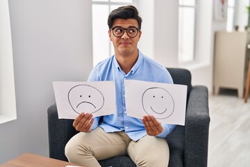 Sticker - Hispanic man working on depression holding sad to happy emotion paper smiling looking to the side and staring away thinking.