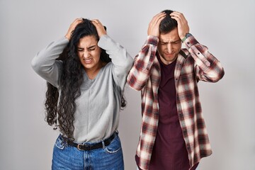 Wall Mural - Young hispanic couple standing over white background suffering from headache desperate and stressed because pain and migraine. hands on head.