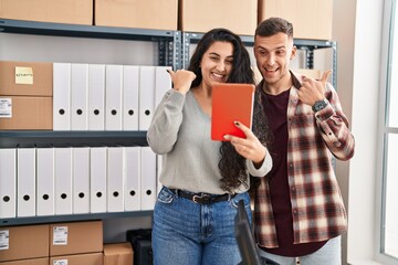 Poster - Young hispanic couple working at small business ecommerce doing video call pointing thumb up to the side smiling happy with open mouth