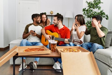 Wall Mural - Group of young friends having party eating italian pizza and playing classical guitar at home.