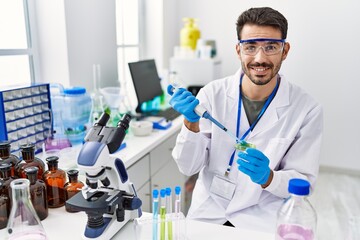 Wall Mural - Young hispanic man wearing scientist uniform using pipette at laboratory