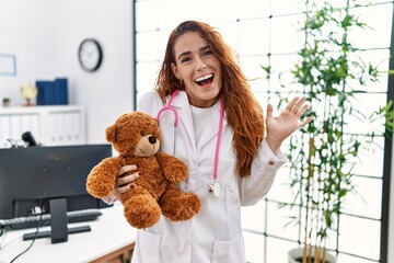 Poster - Young redhead pedriatician woman holding teddy bear celebrating achievement with happy smile and winner expression with raised hand